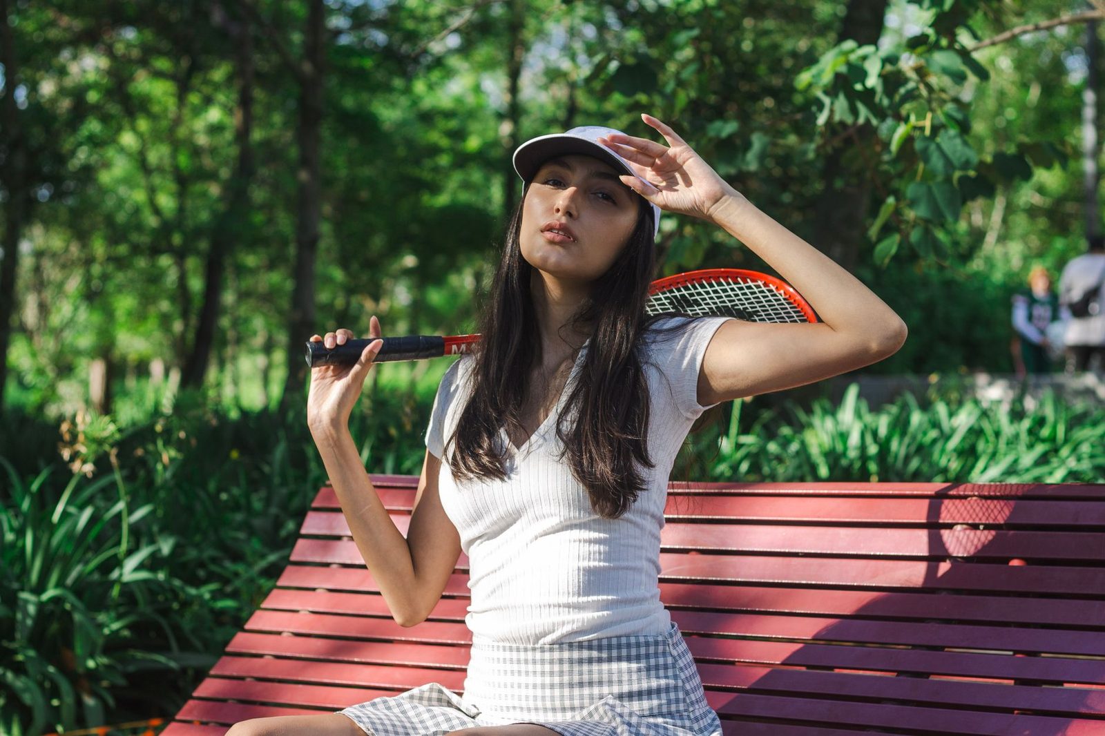 A woman resting on an outdoor bench with a tennis racquet