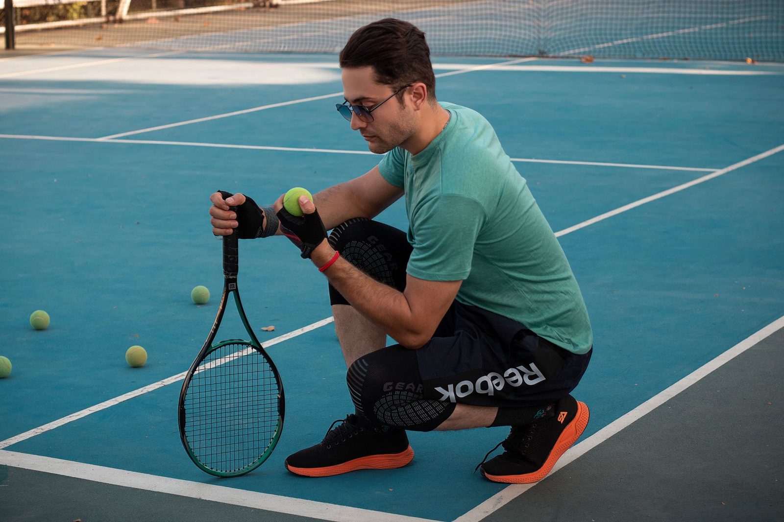Tennis player crouching low on court holding a racquet and balls