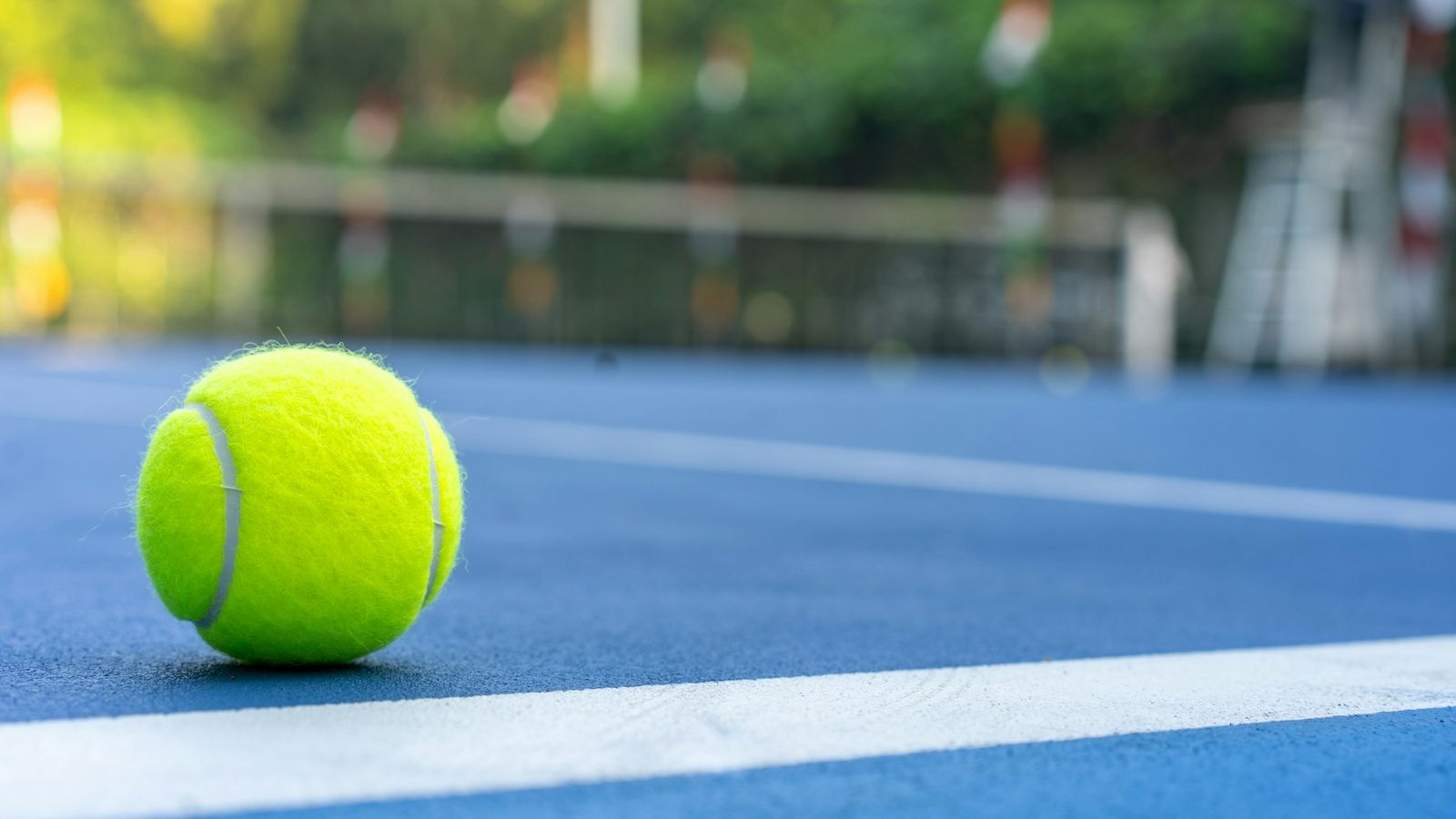 Bright yellow tennis ball resting on a blue hard court