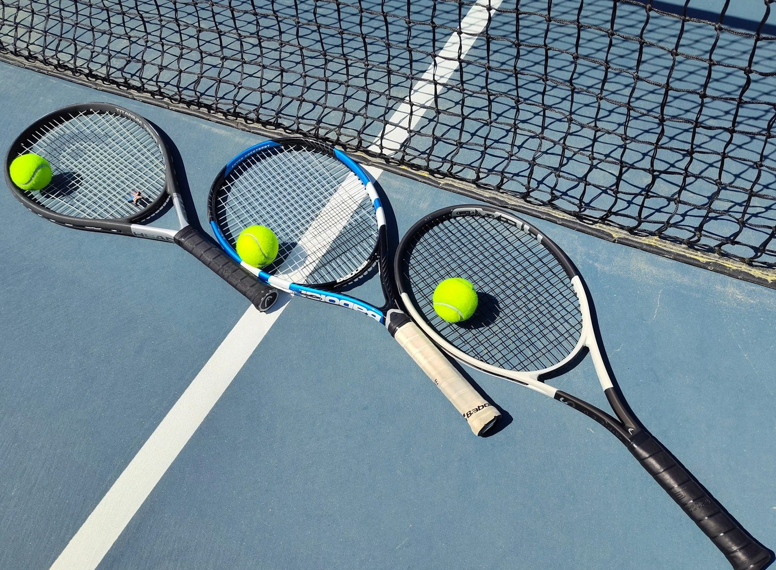 Two tennis racquets and two balls resting together on a court surface