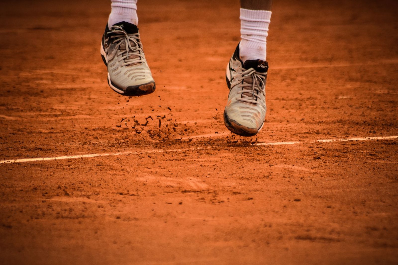 Close view of a player's shoes mid-jump on a clay tennis court