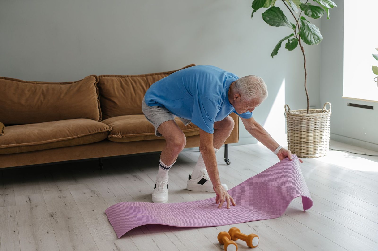 An older man setting up a yoga mat for an indoor exercise session