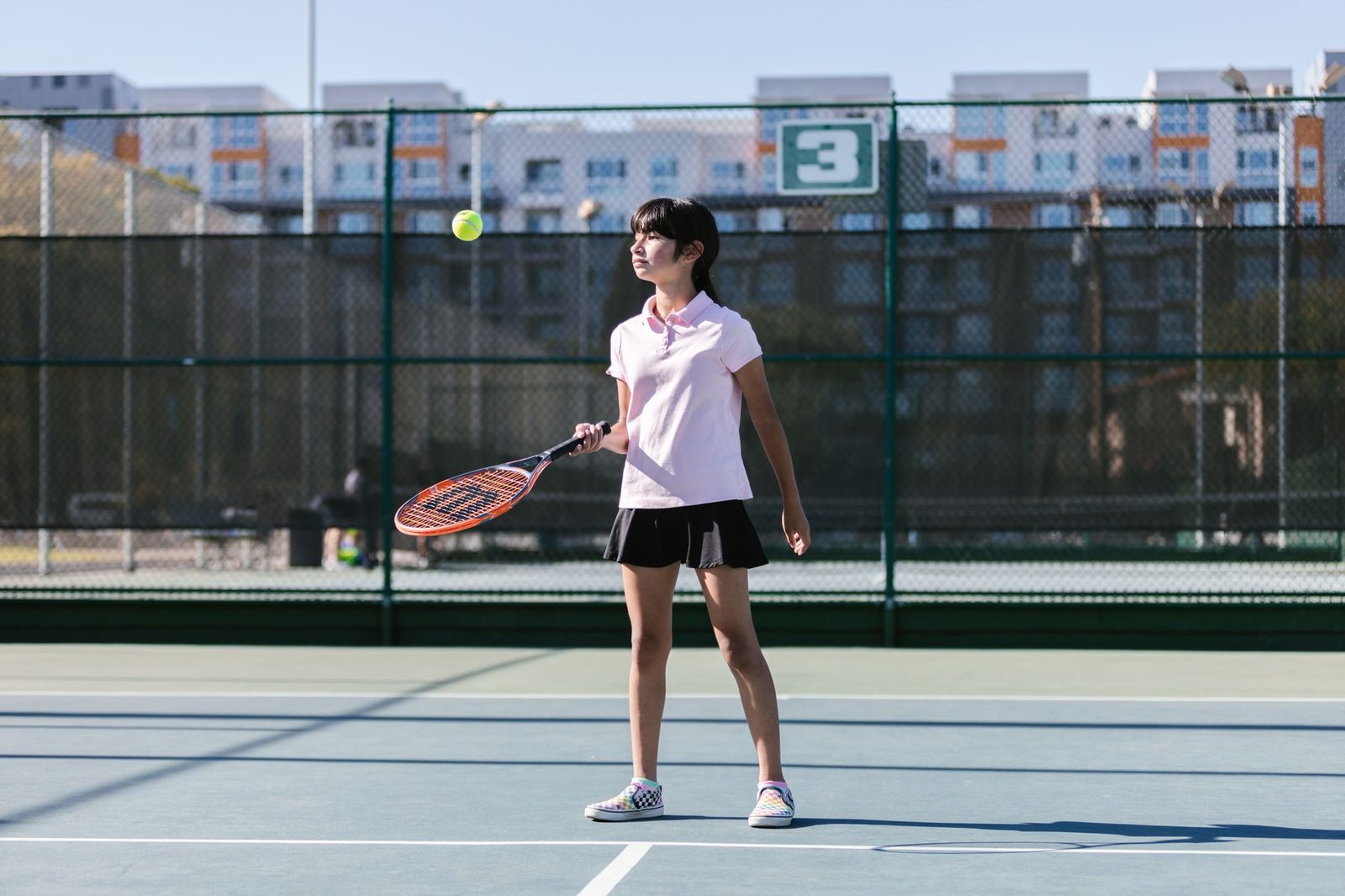 A young girl practising tennis outdoors on a sunny day