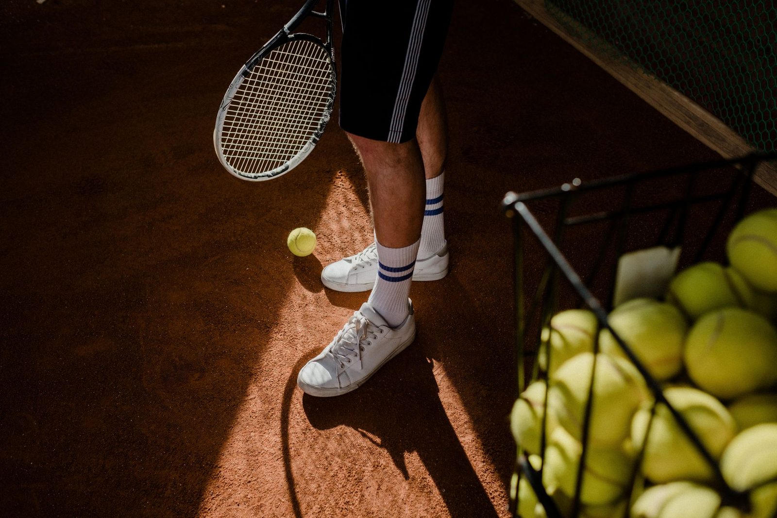 A player standing on a clay court with racquet, shoes and balls in sunlight
