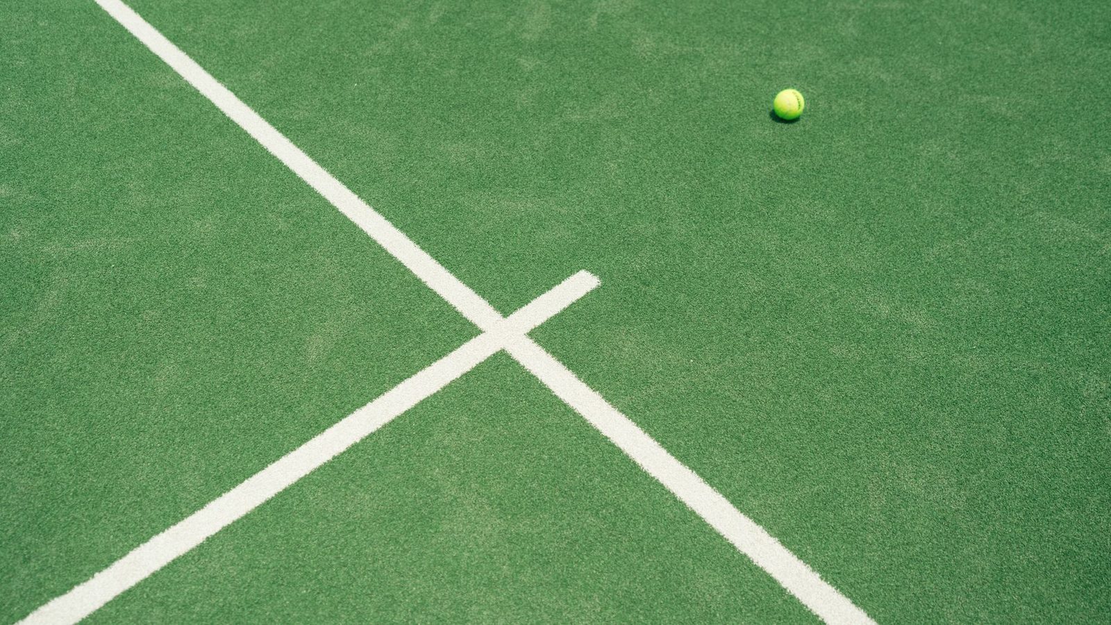 A tennis ball lying on a green court beside the white lines