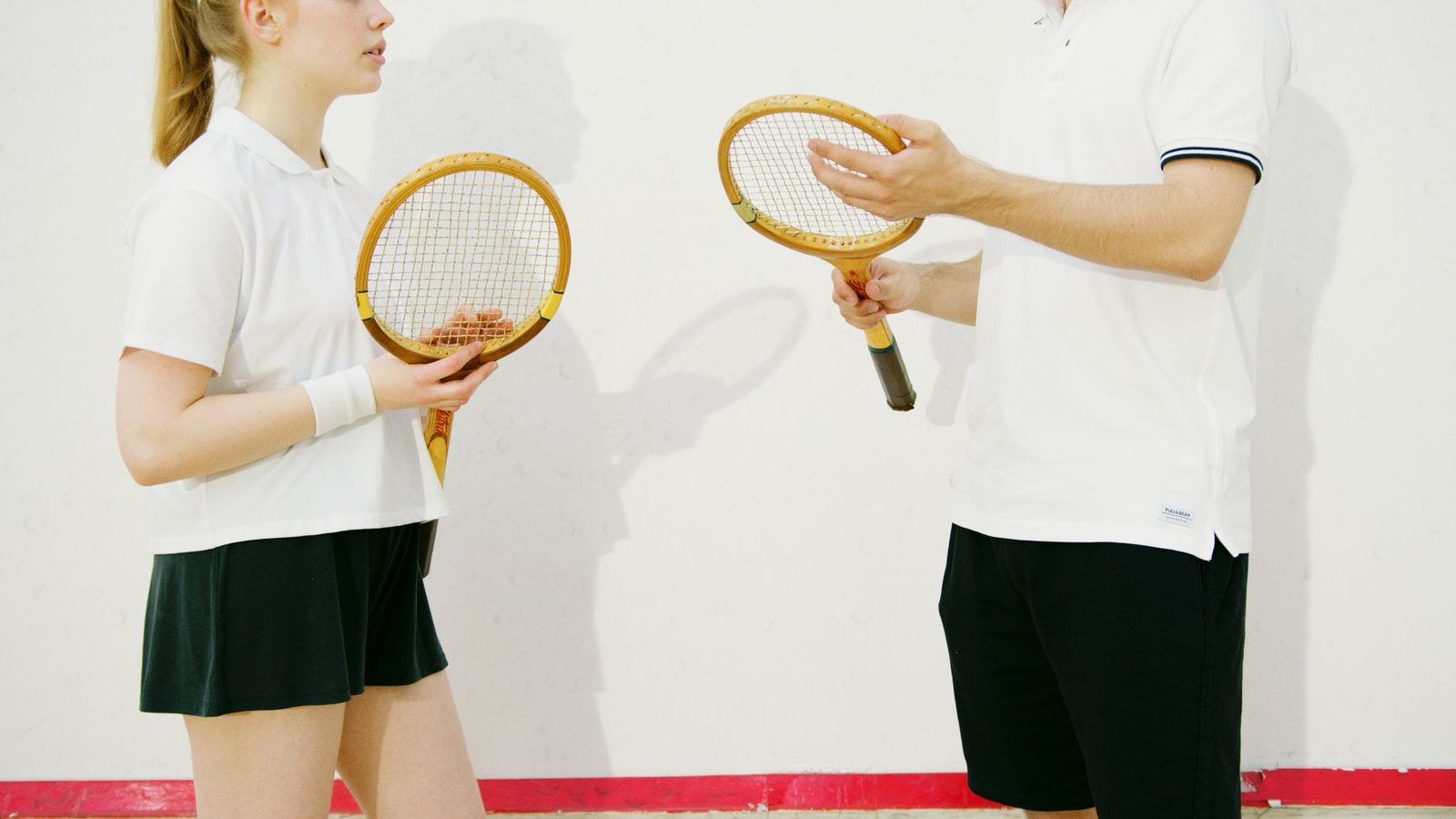 Two adults holding wooden tennis racquets indoors