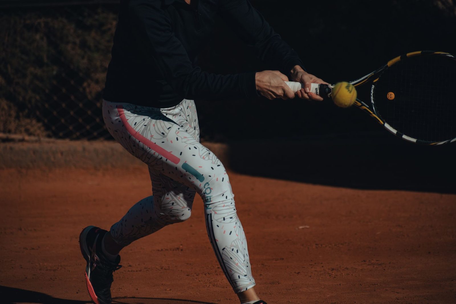 Woman hitting a backhand on a clay court, focused on the ball