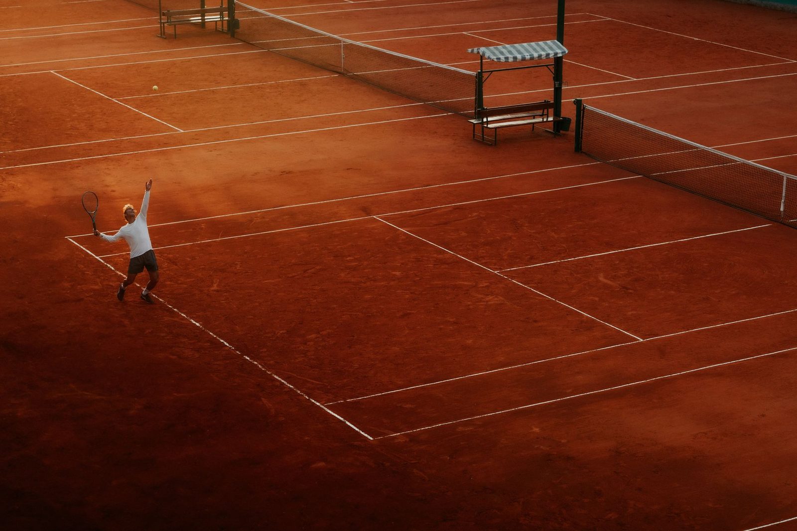A player serving on a clay tennis court at sunset
