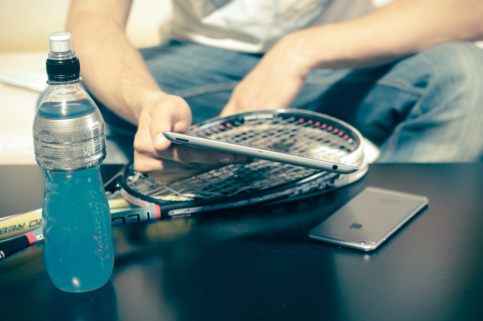 A person sitting beside a tennis racquet and a drink