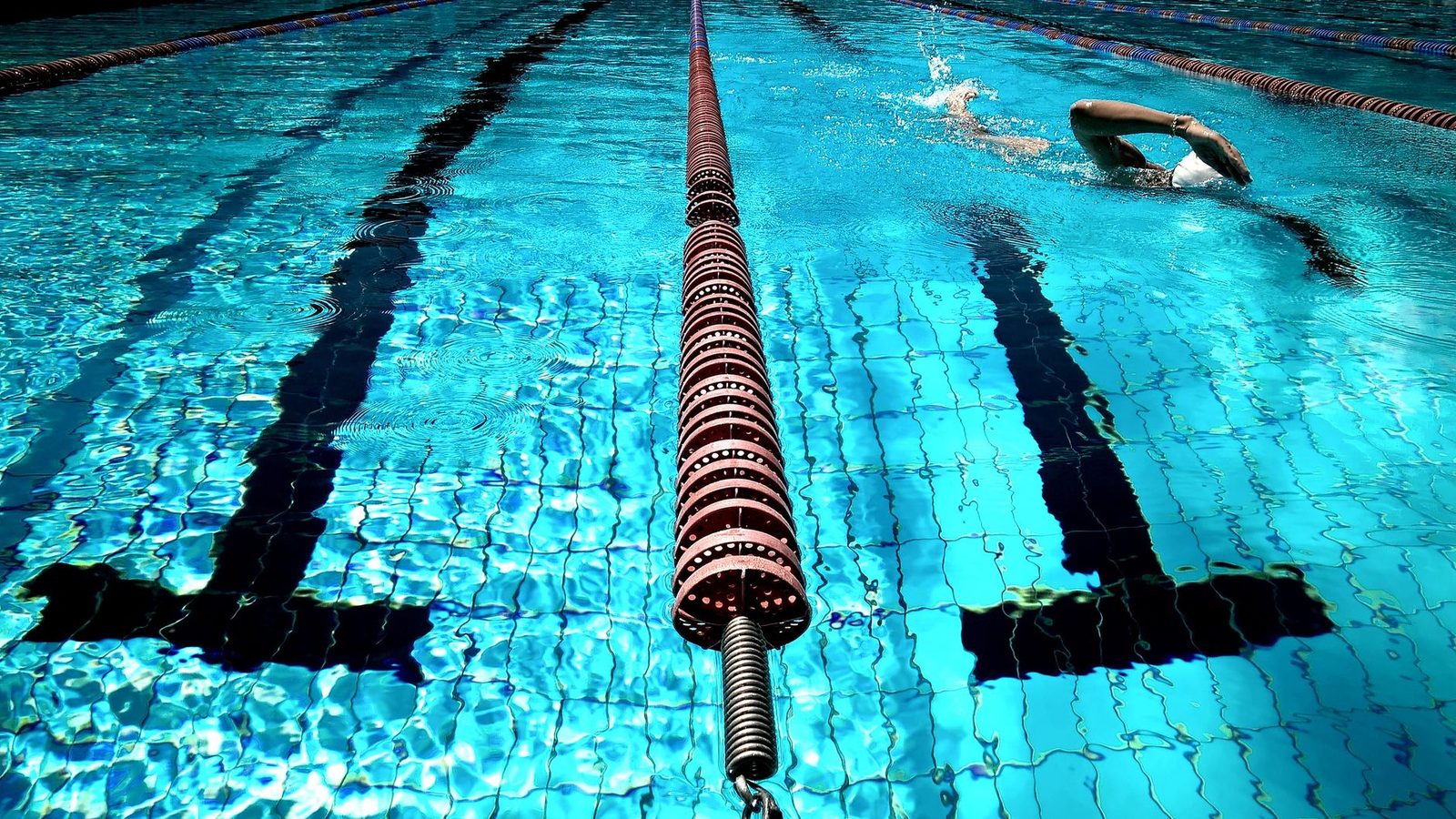 A person swimming in an outdoor pool with lane dividers