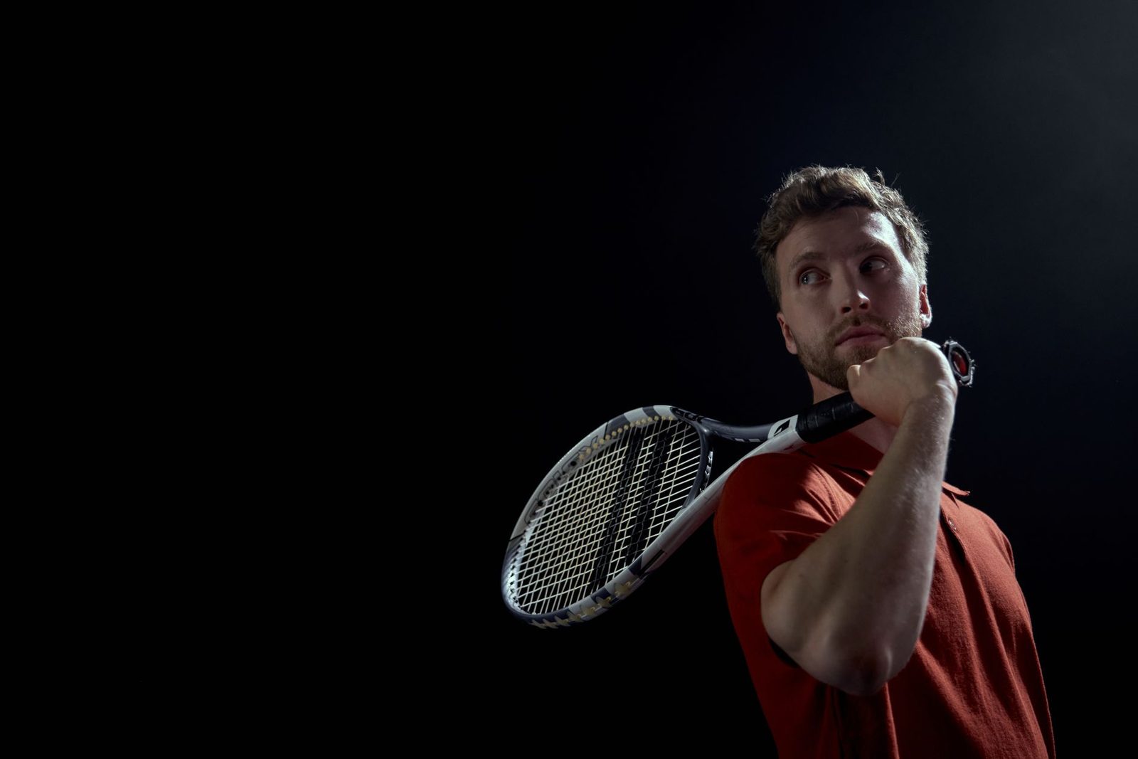 A tennis player holding a racquet against a dark background