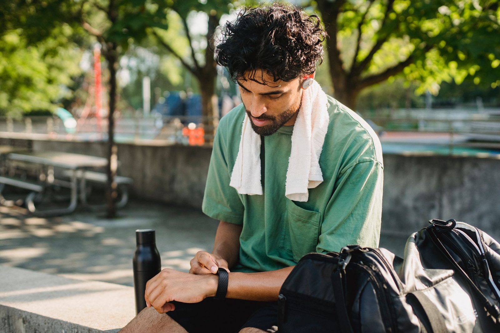 A man resting on a bench after a workout with a towel and water bottle