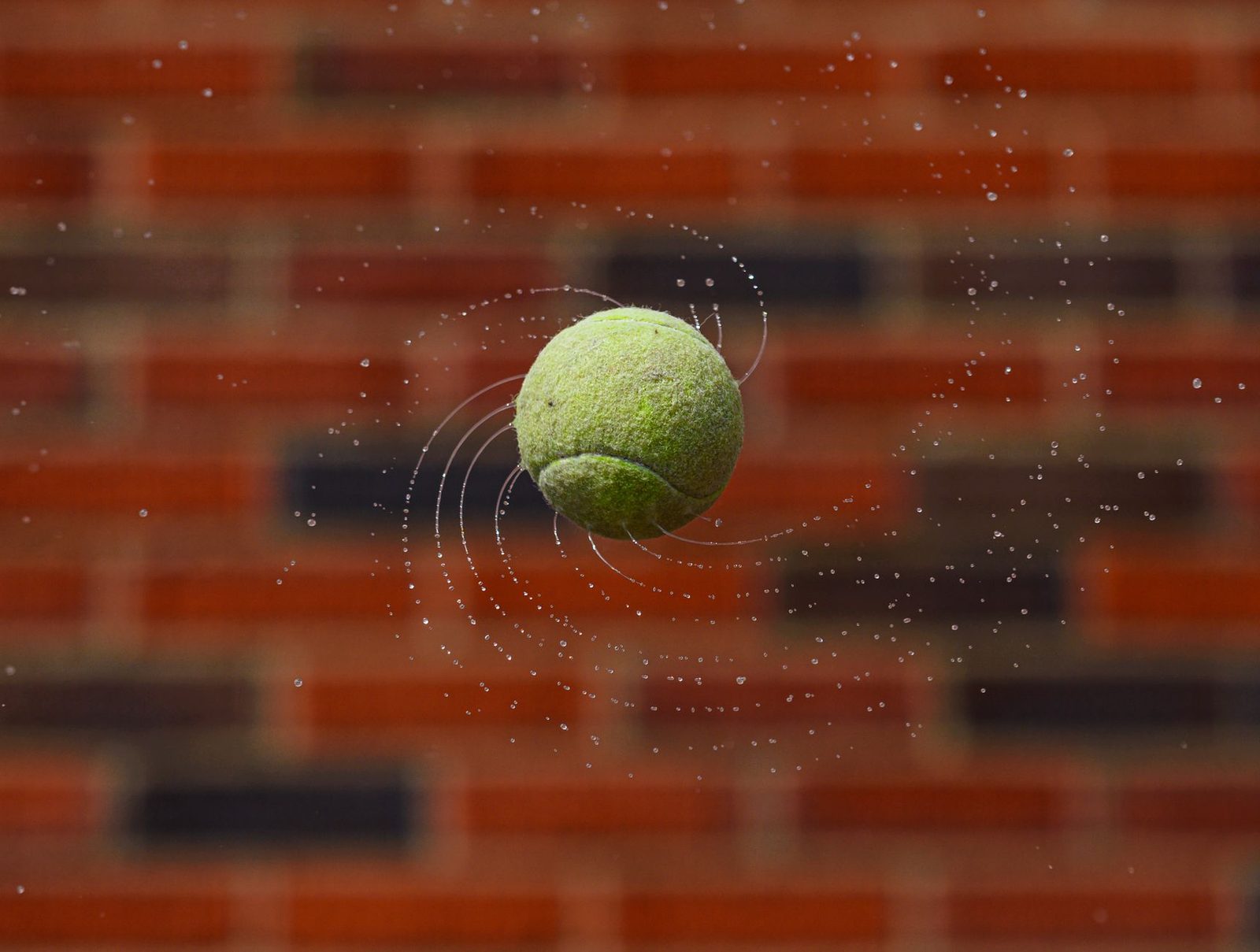 A tennis ball in motion against a brick wall