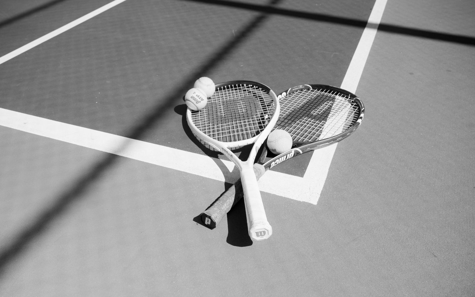 Two racquets and tennis balls laid out on a sunlit court before a practice session