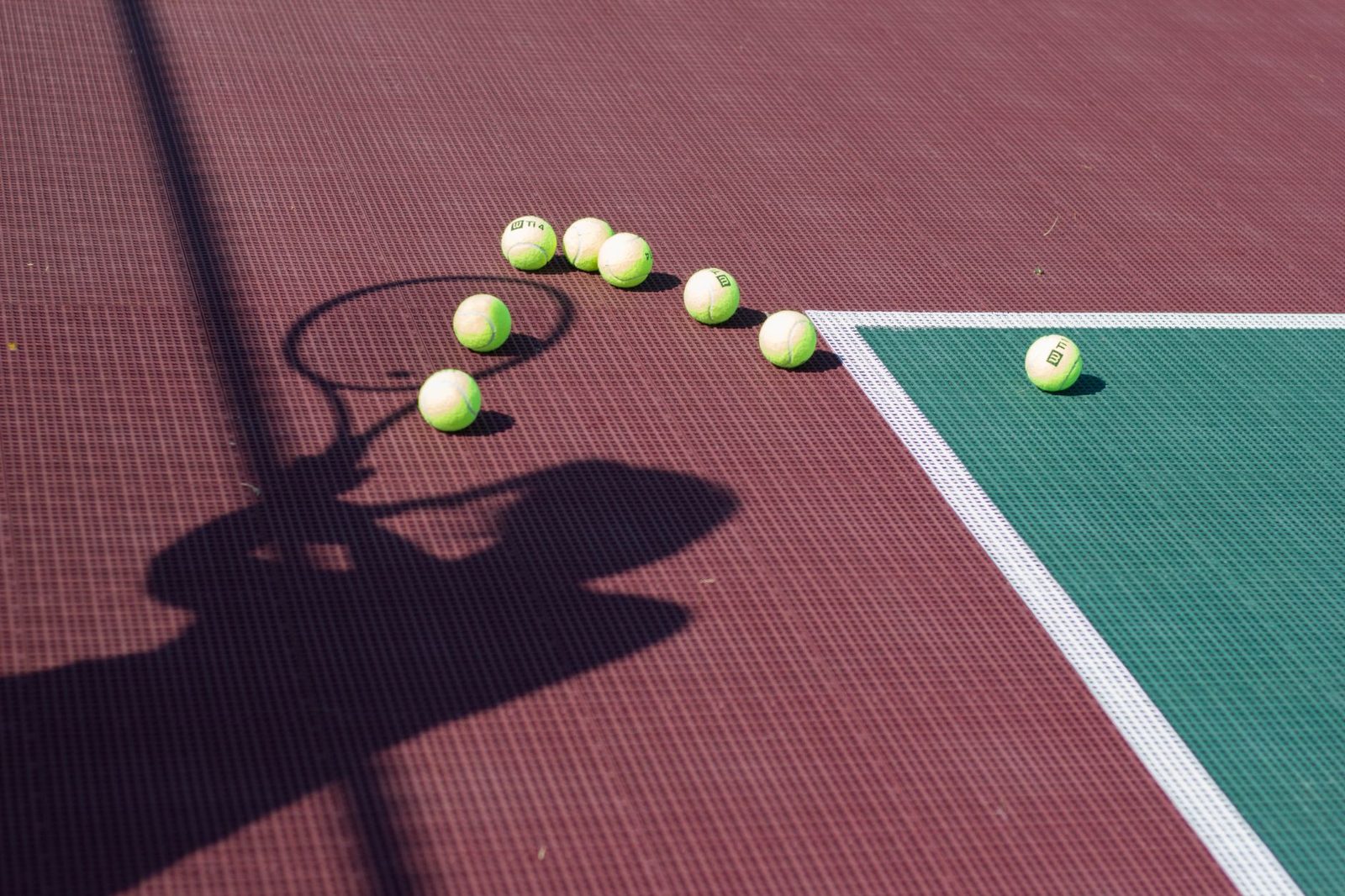 A racquet's shadow and scattered tennis balls on a sunlit court