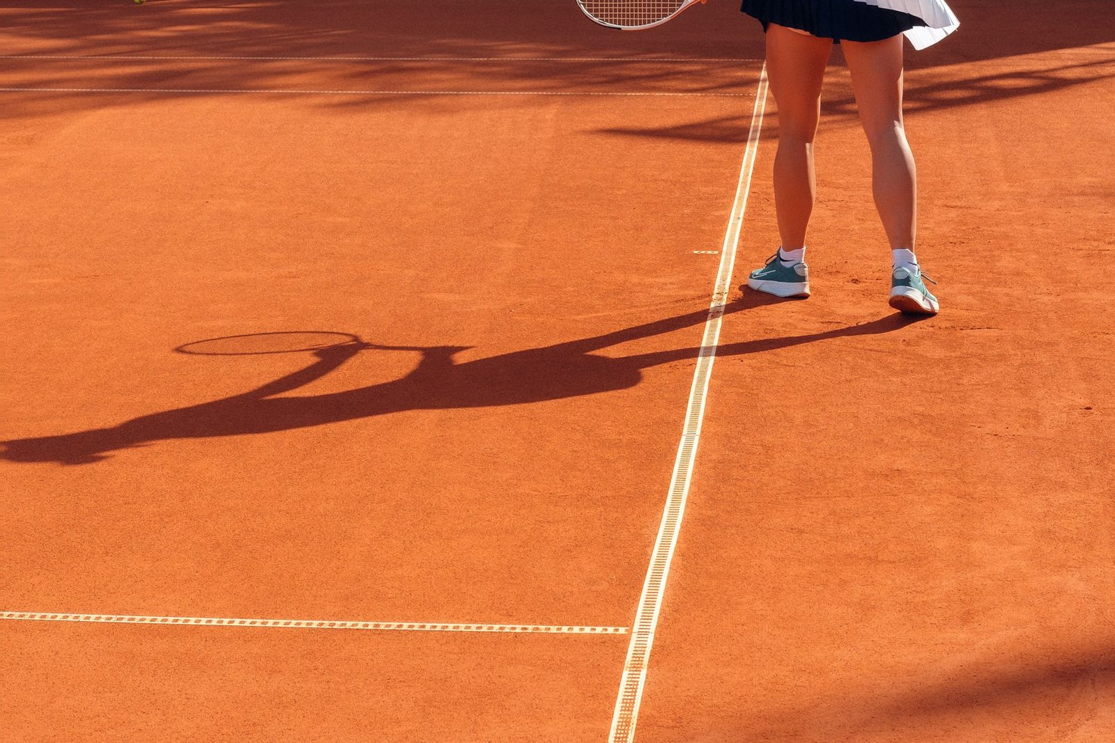 Tennis player on a clay court casting a long shadow