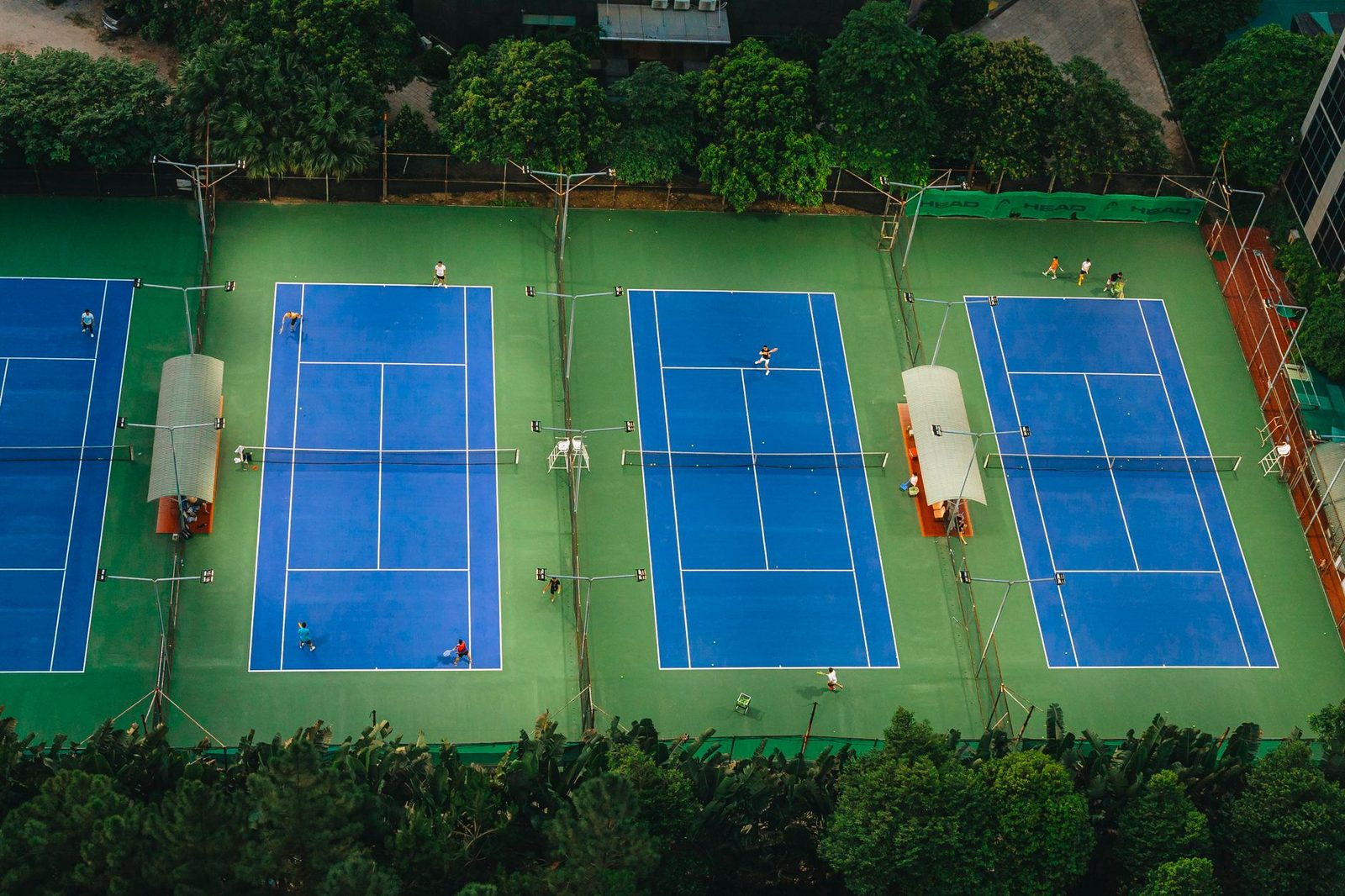 Tennis courts from above with players in action, surrounded by greenery