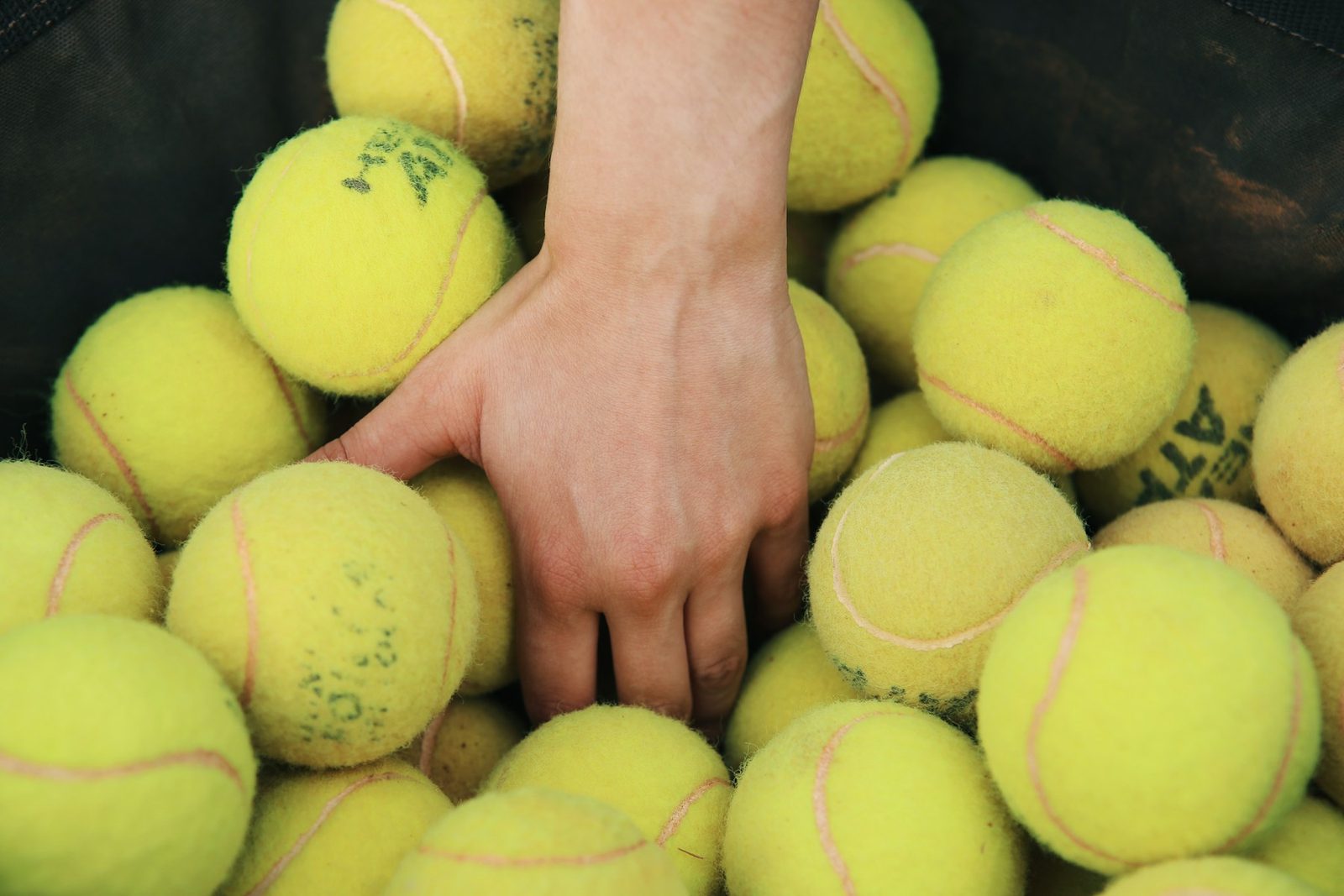 A person reaching for a tennis ball in a ball bin