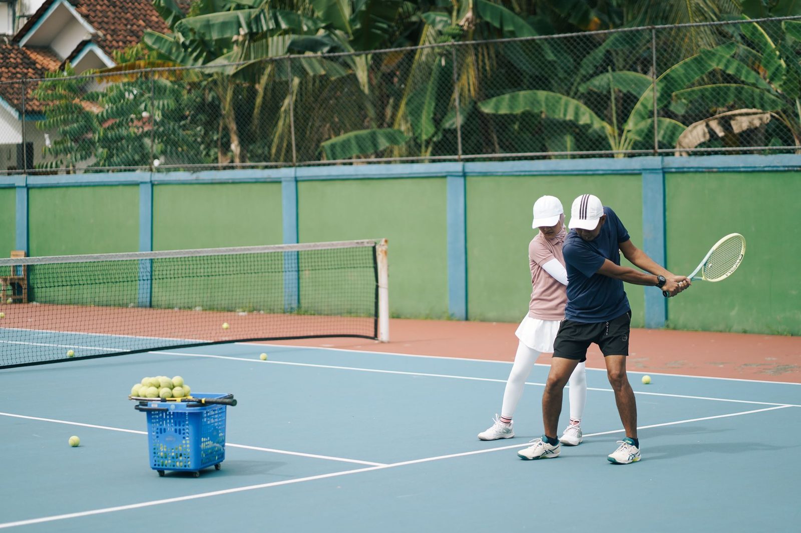 Coach instructing a player during a tennis lesson on a sunny outdoor court