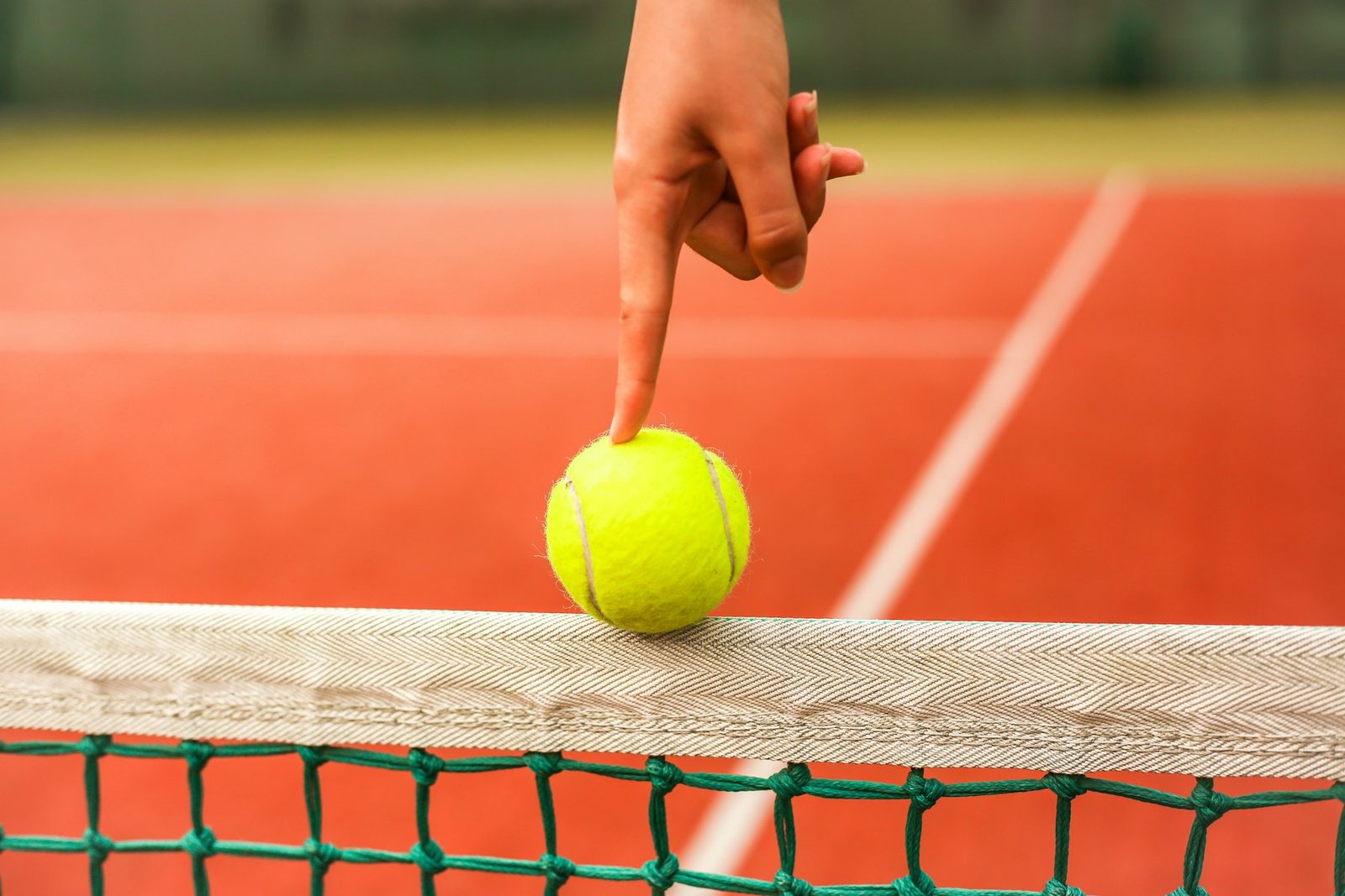 Player resting a yellow tennis ball on the net cord between drills