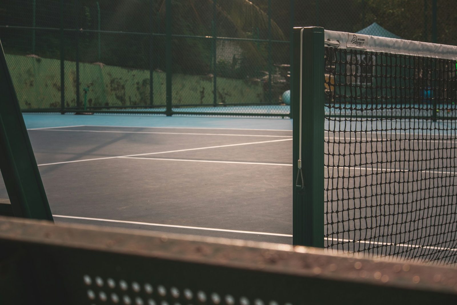 Two players on a fenced outdoor tennis court seen through the perimeter fencing