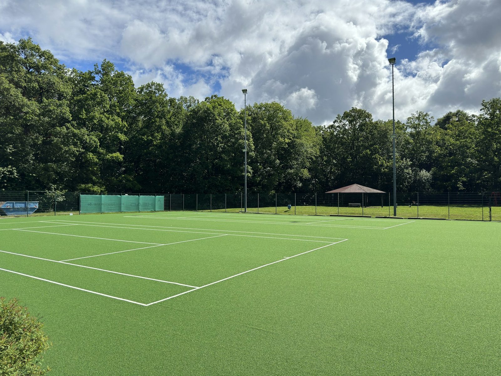 A tennis court surrounded by trees under a blue sky