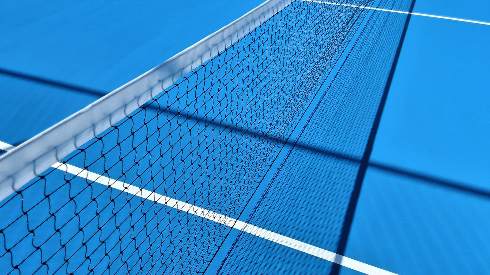 Blue hard tennis court with the net and shadows in sunlight