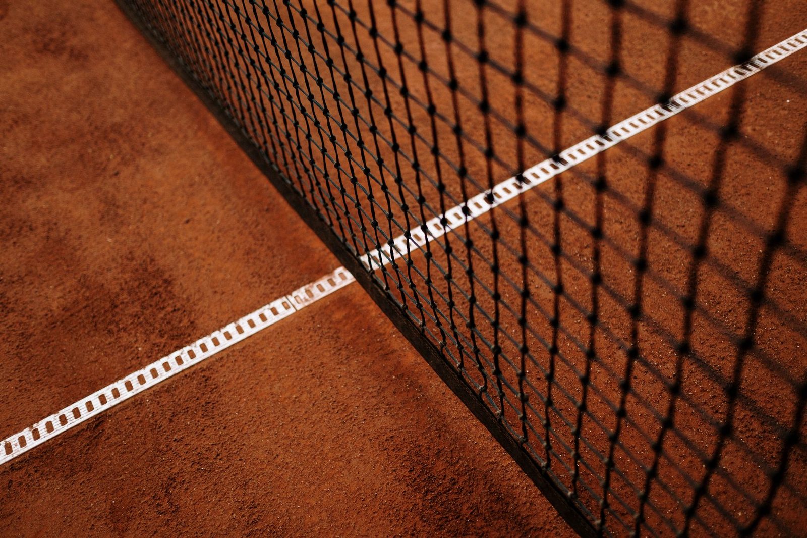 Close view of a clay tennis court showing the net and white baseline