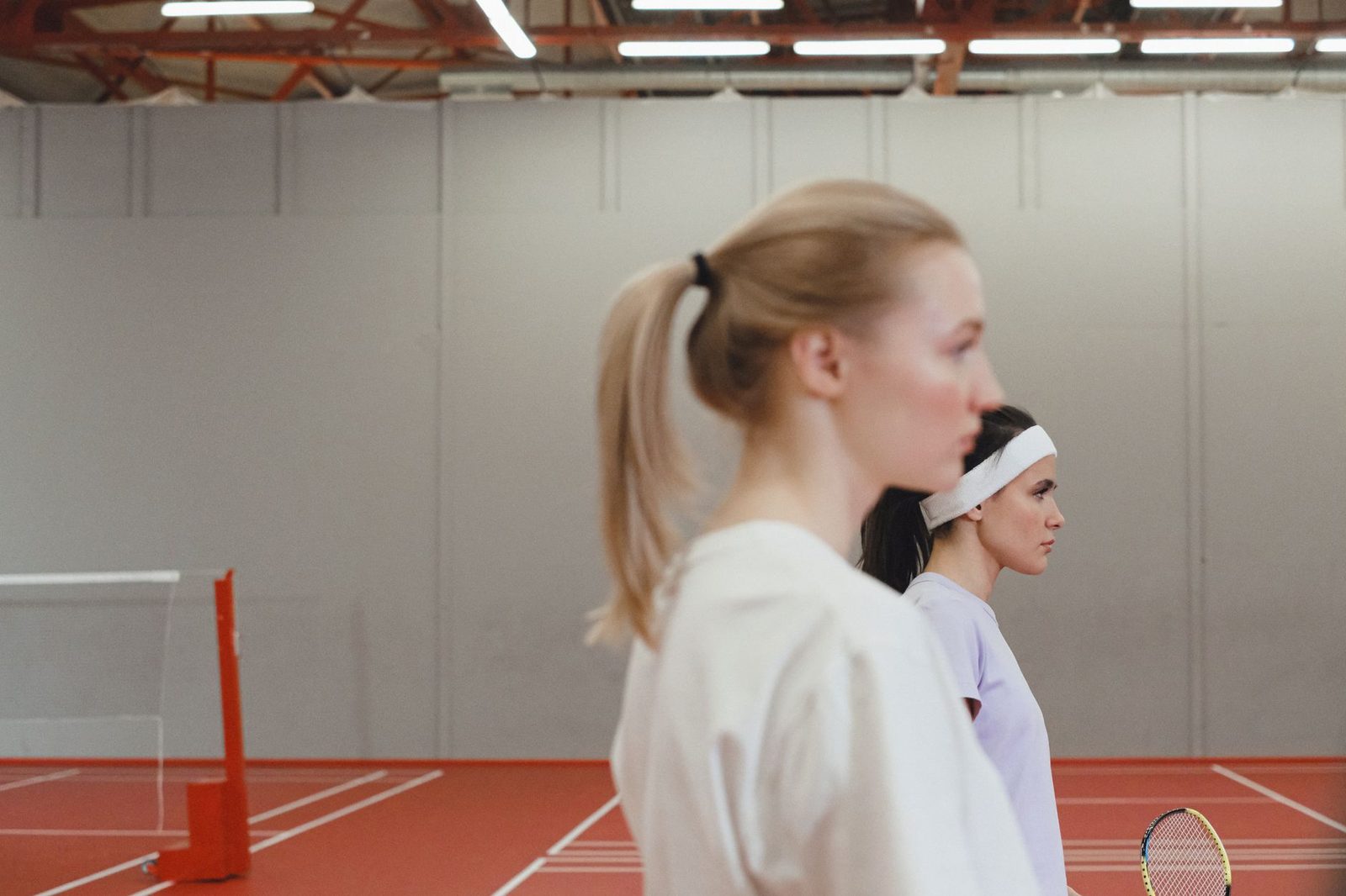 Two women playing tennis indoors, focused and ready for the next ball