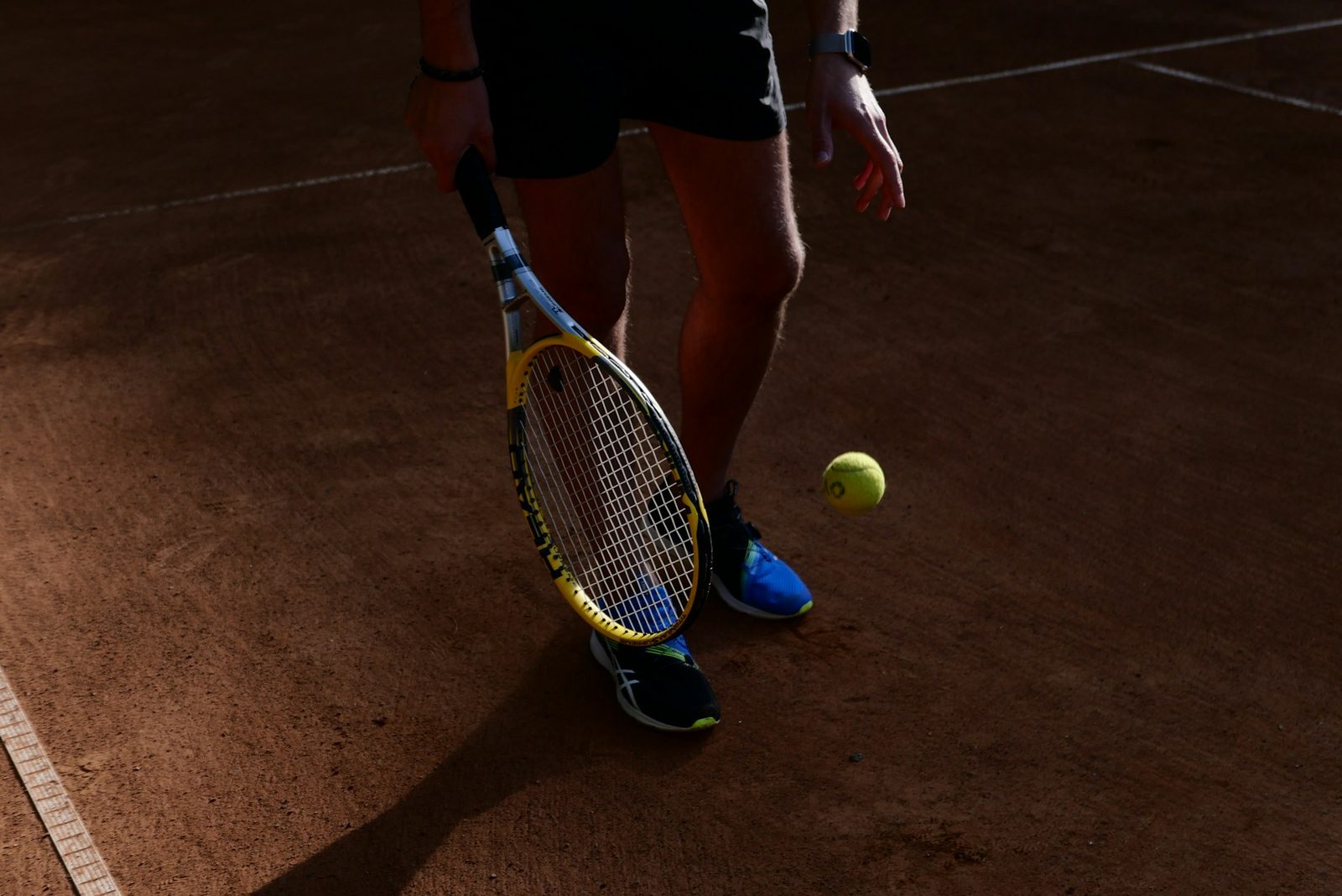 A player's legs, tennis shoes and racquet on a clay court, where all footwork begins