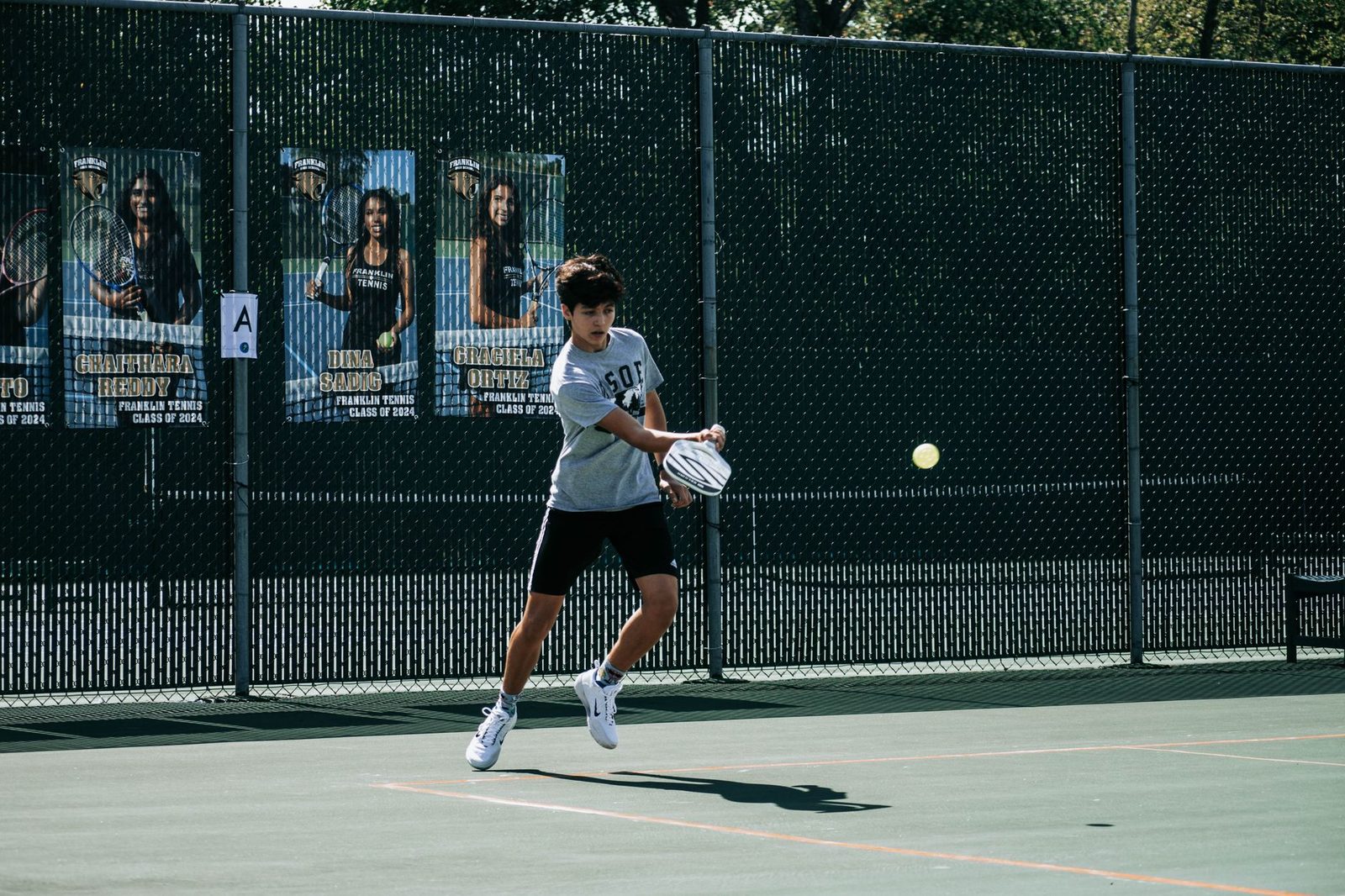 Teenage player striking the ball on an outdoor tennis court
