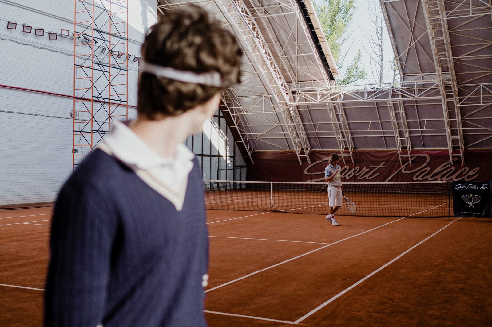 Tennis players moving across an indoor clay court during a competitive match