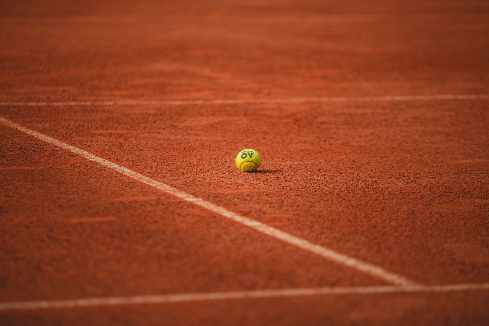 A lone tennis ball resting on a red clay court