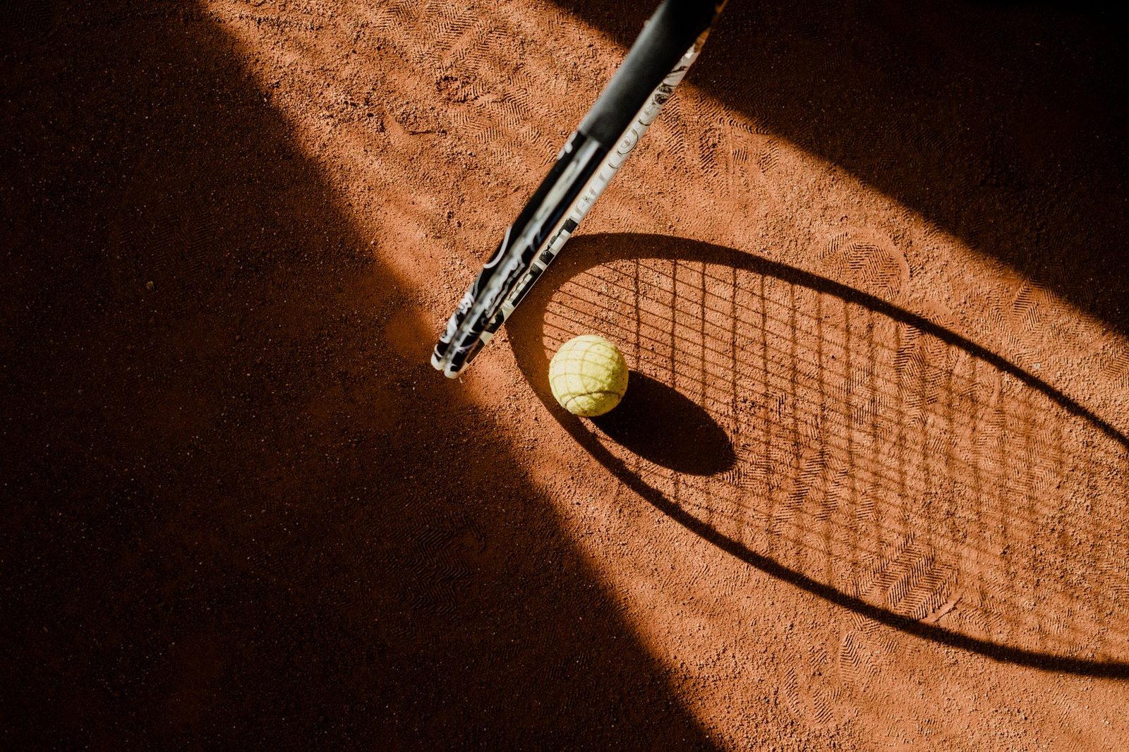 Tennis ball and racquet shadow on a sunlit clay court