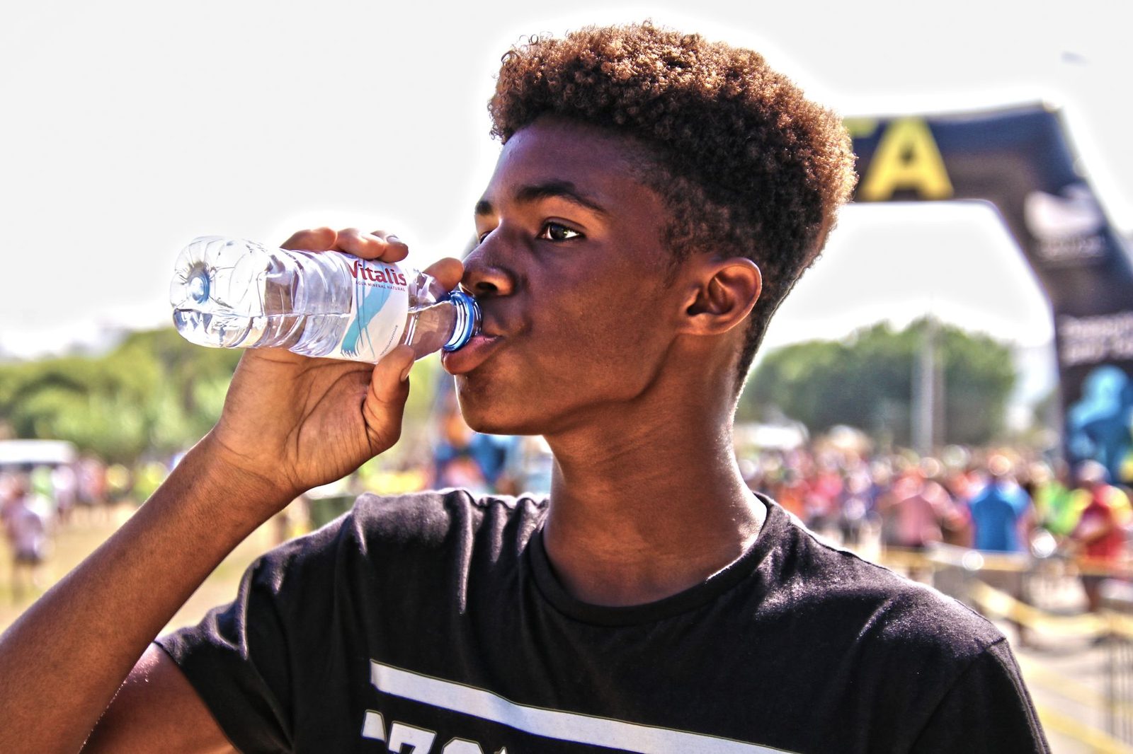 A young man drinking bottled water outdoors at a sporting event