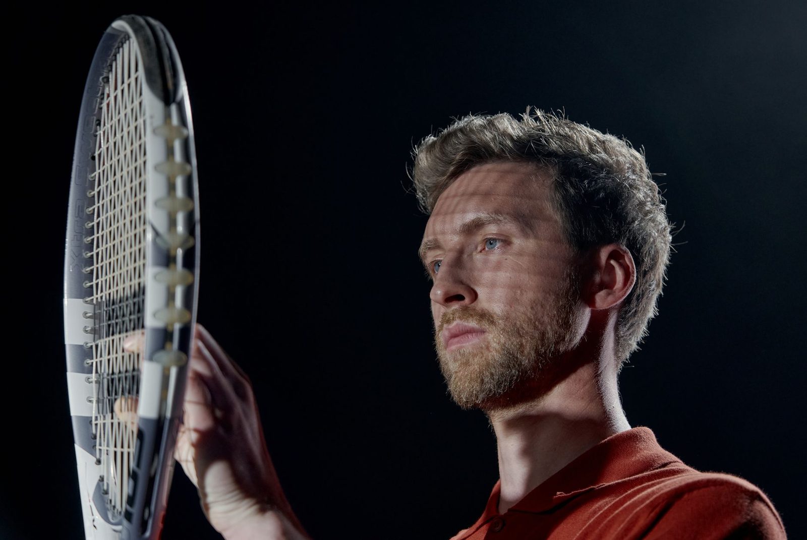 Portrait of a tennis player holding a racquet against a dark background