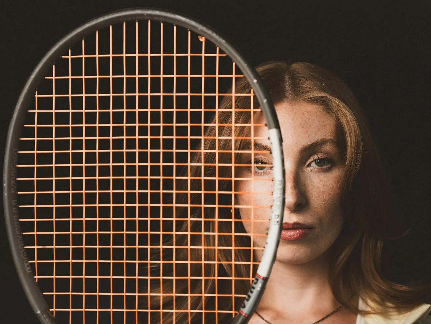 Tennis player holding a racquet up to the camera, seen through the string bed