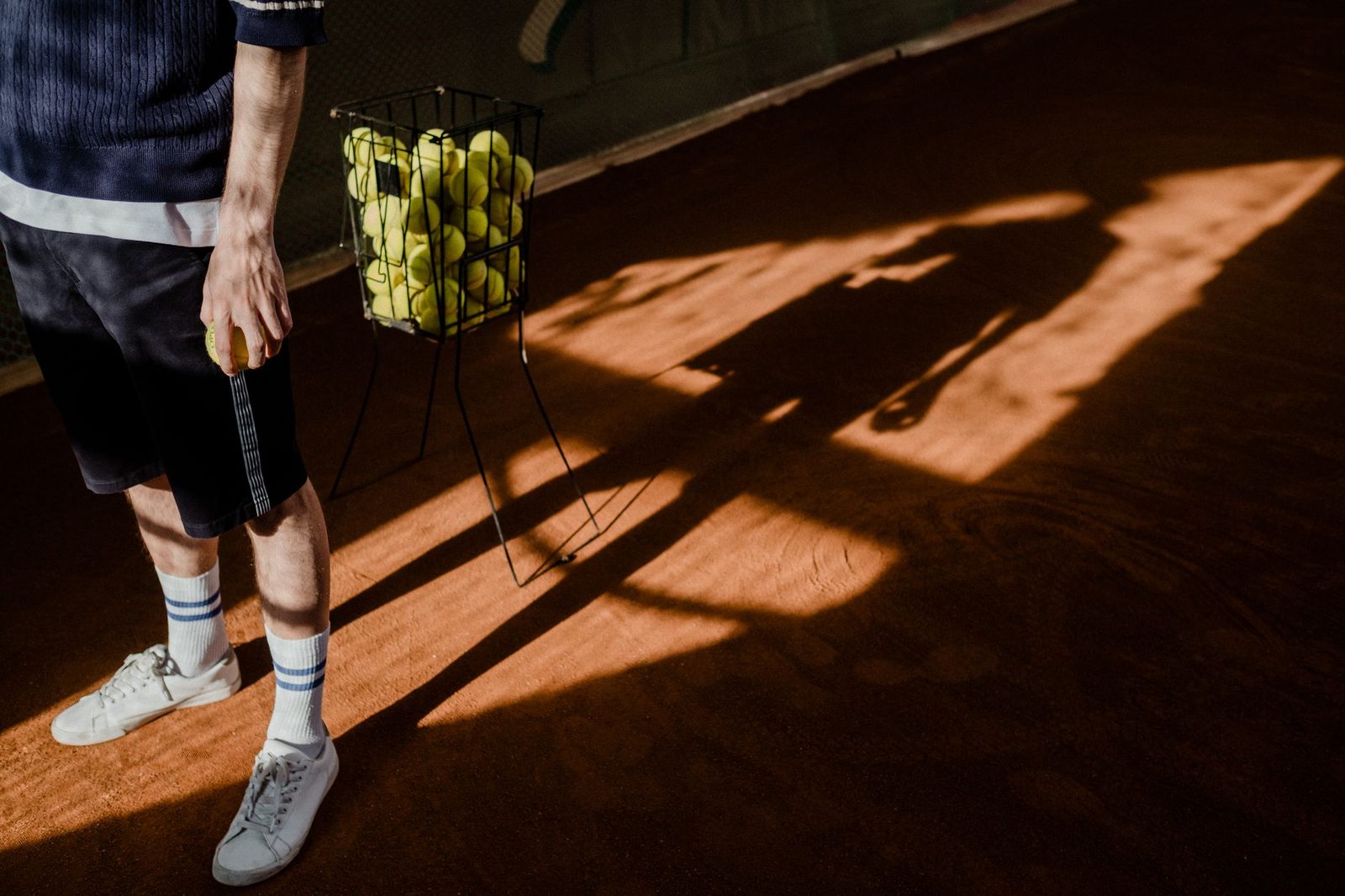 Long shadow of a tennis player training alone on a clay court