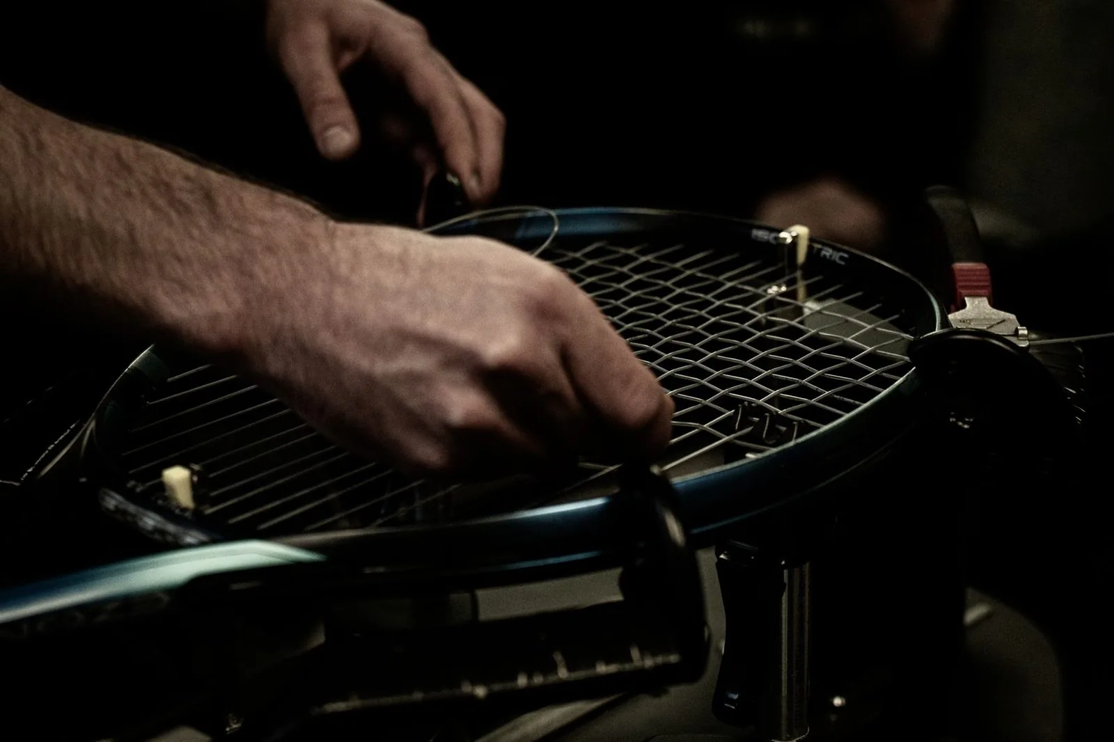 Tennis racquet mounted on a stringing machine while a stringer works across the string bed