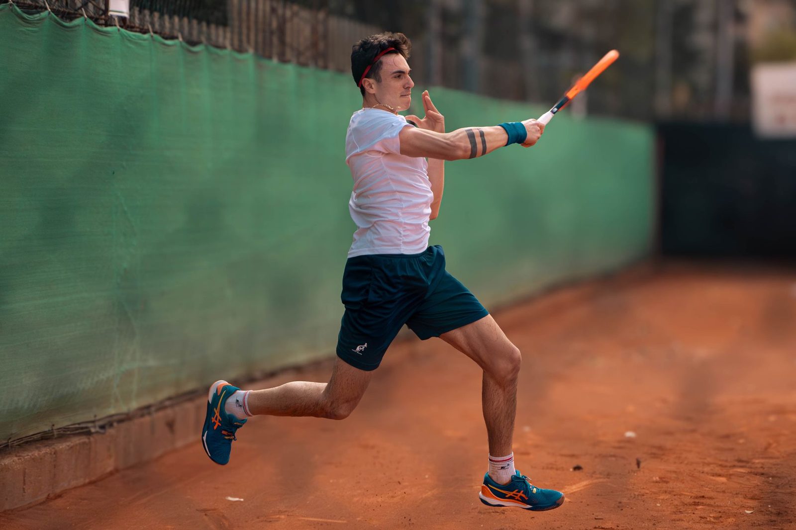 A focused tennis player mid-swing on a clay court