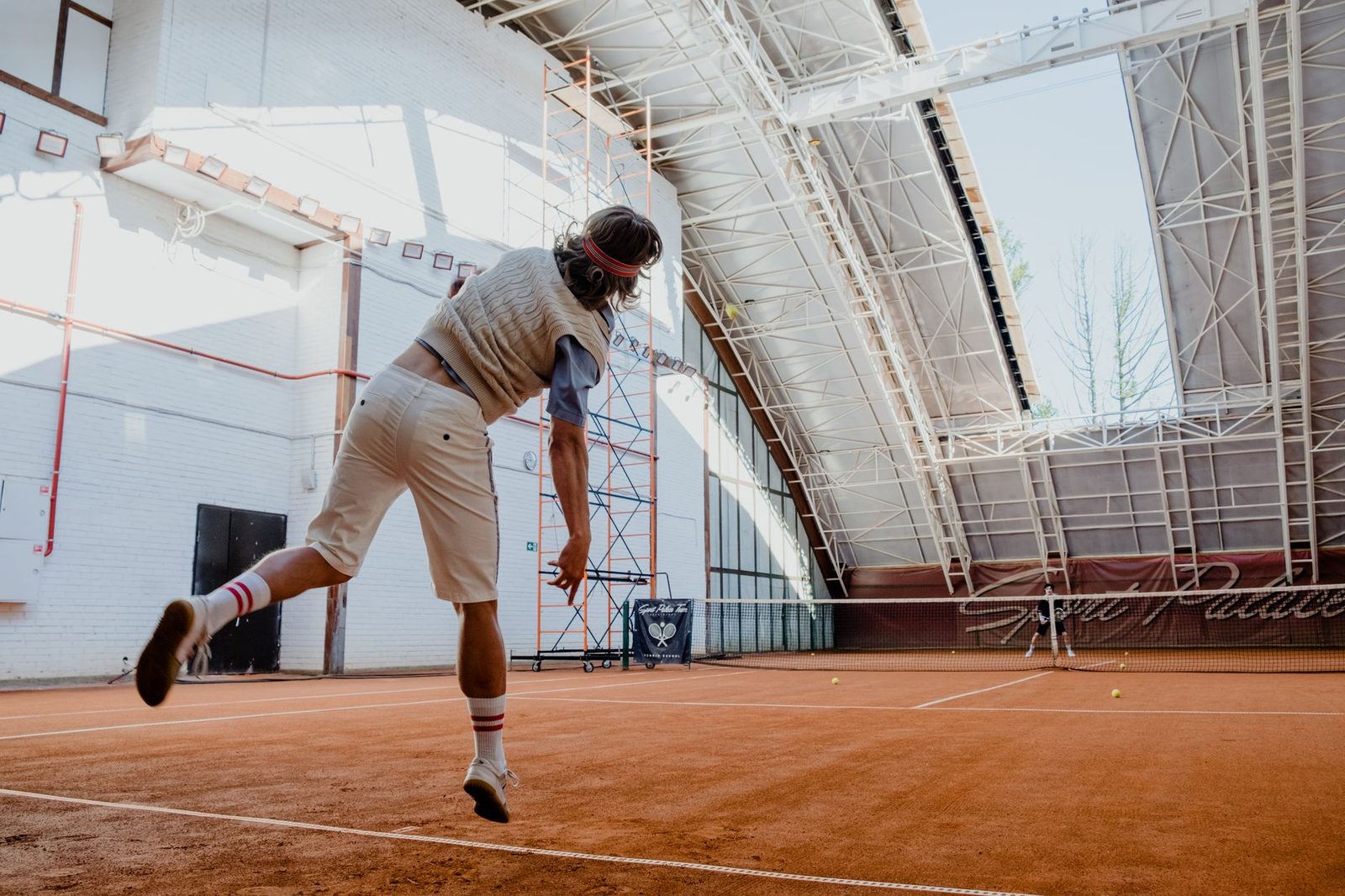 Back view of a tennis player mid-action on an indoor clay court
