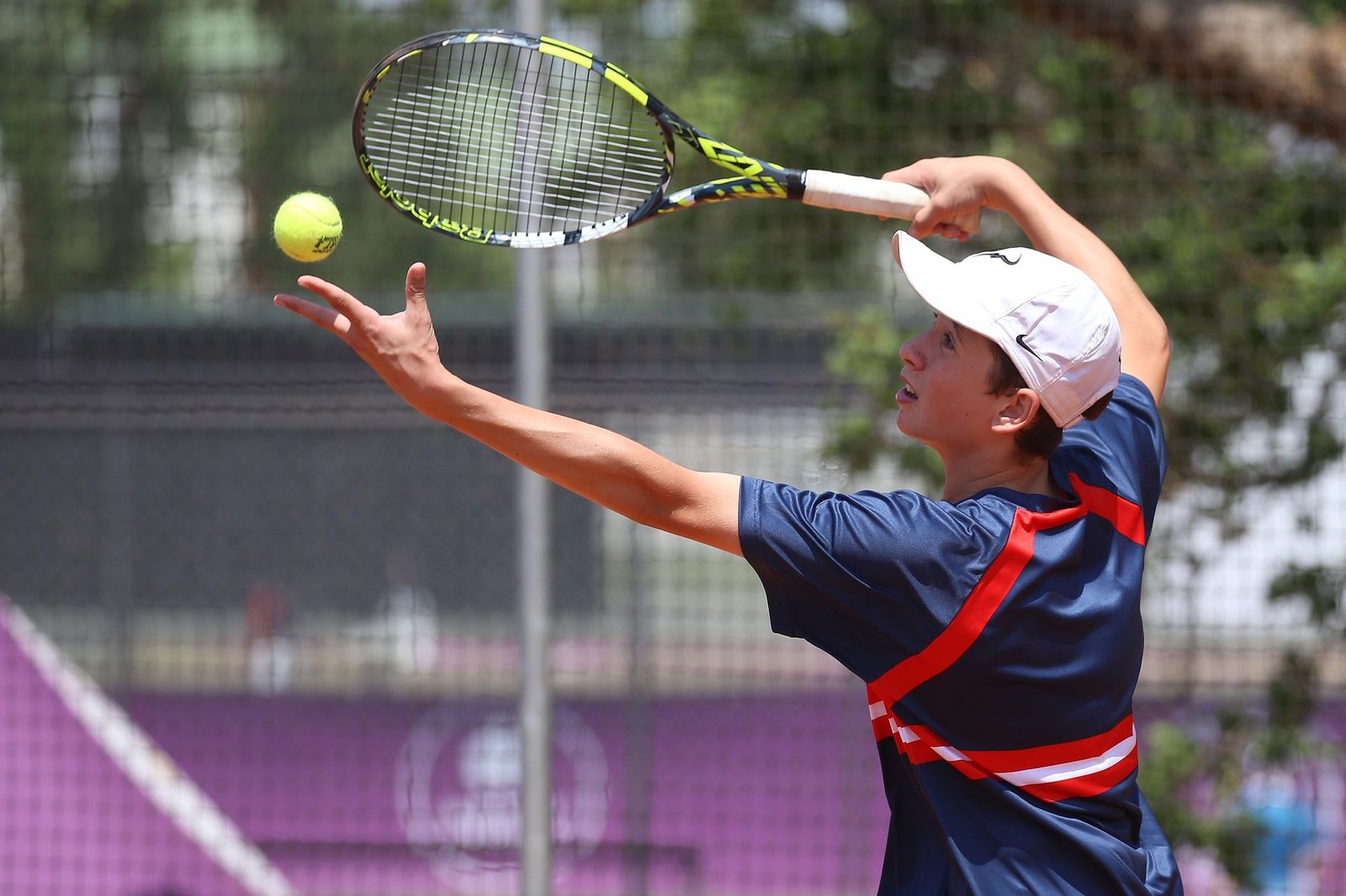 Teenage tennis player mid-serve on a sunny outdoor court
