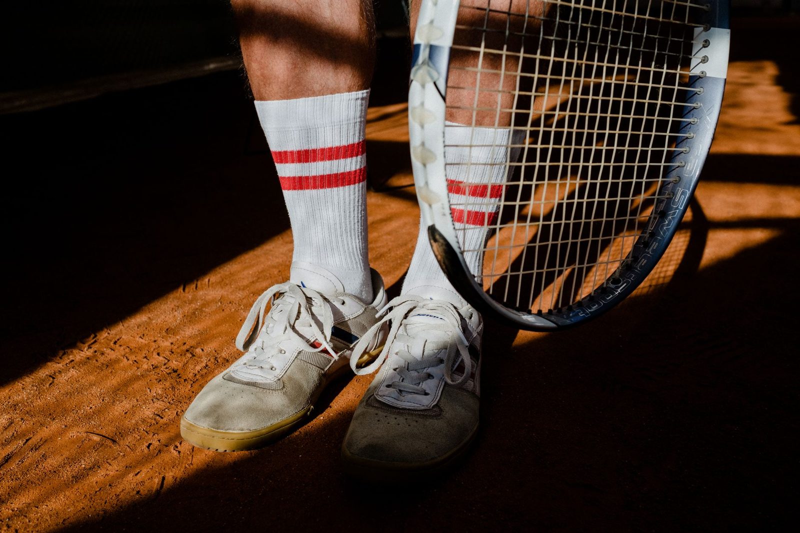 Close view of tennis shoes, socks and a racquet resting on a clay court