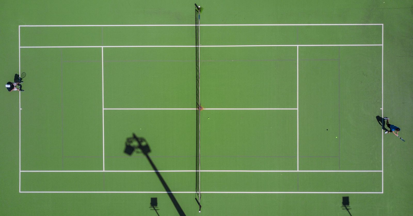 Overhead view of a tennis match in progress on a bright green hard court