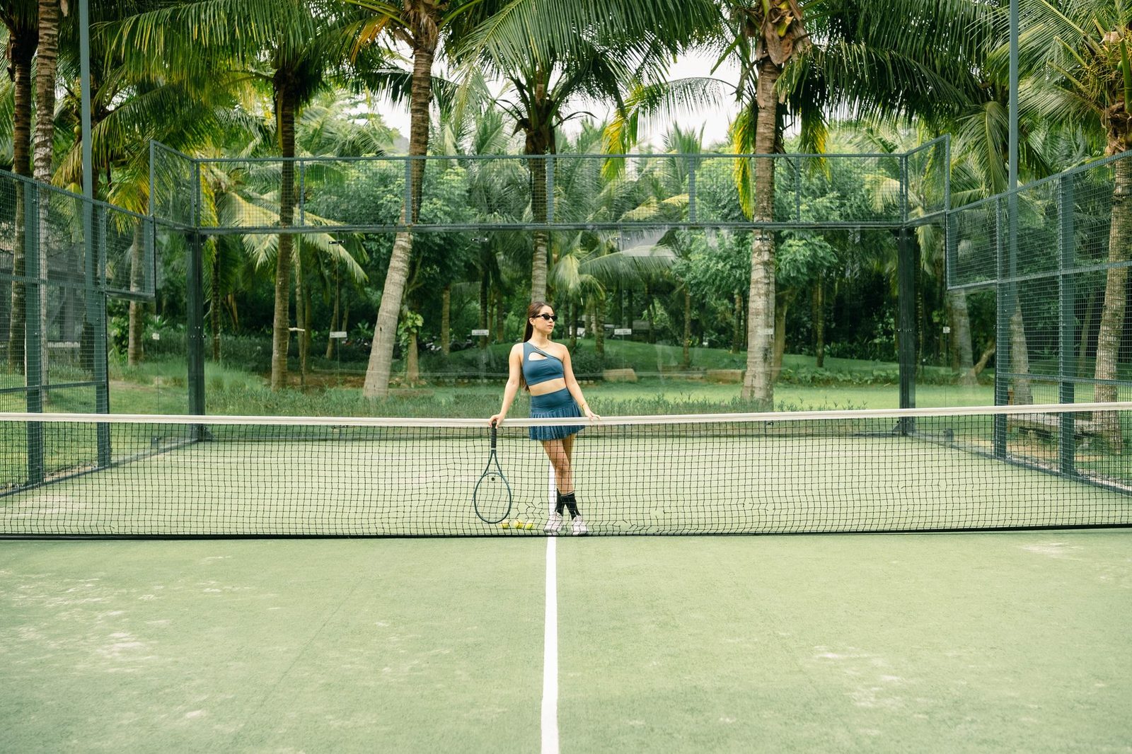 Player standing with a racquet on an outdoor court lined with palm trees