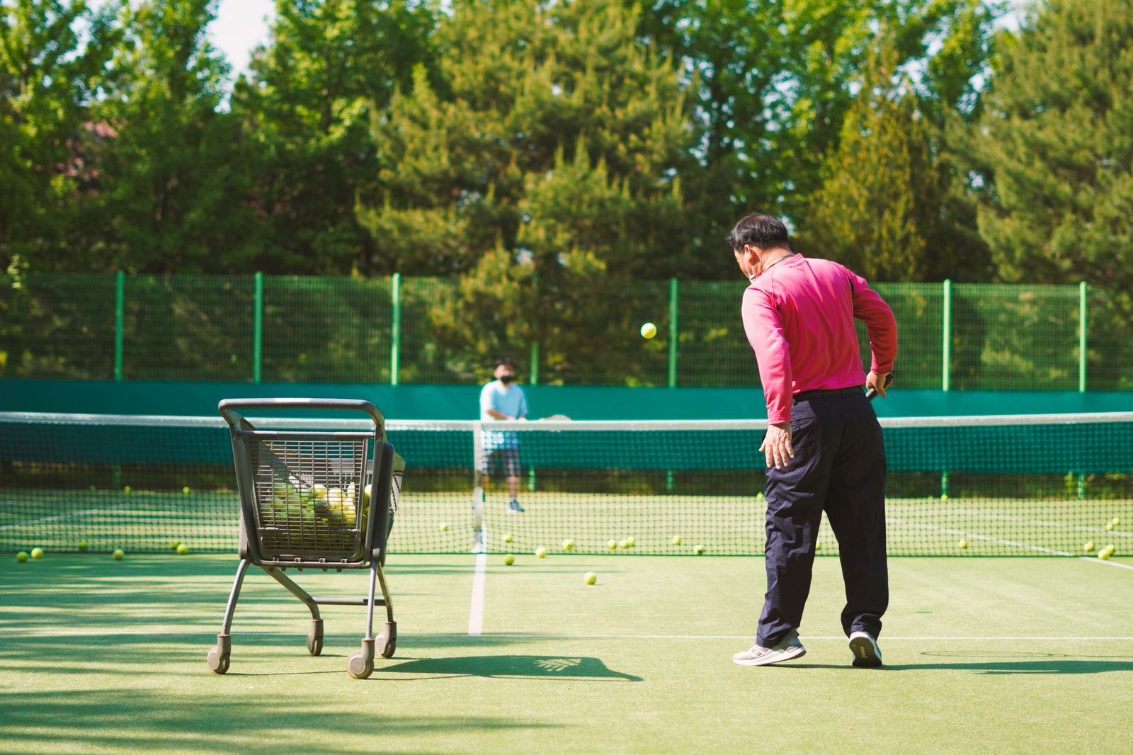Two players practising on a sunny outdoor court beside a ball cart