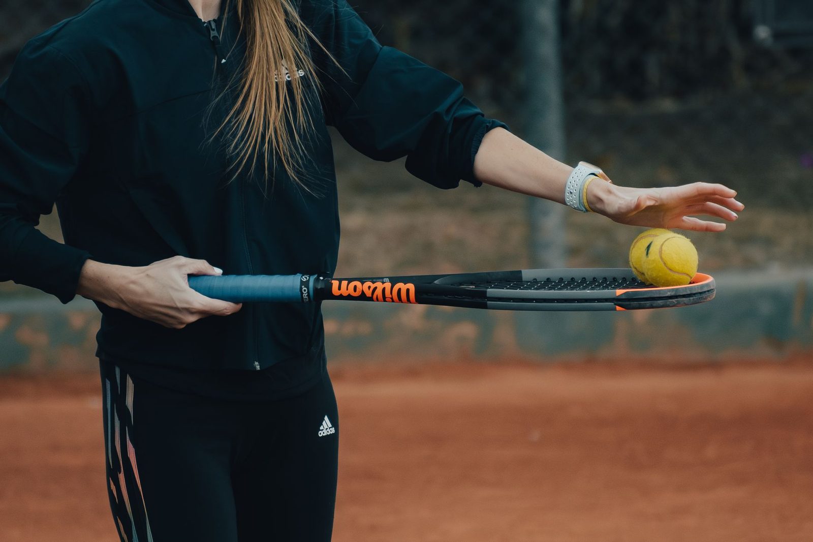 Close view of a woman holding racquet and ball, set to serve on a clay court