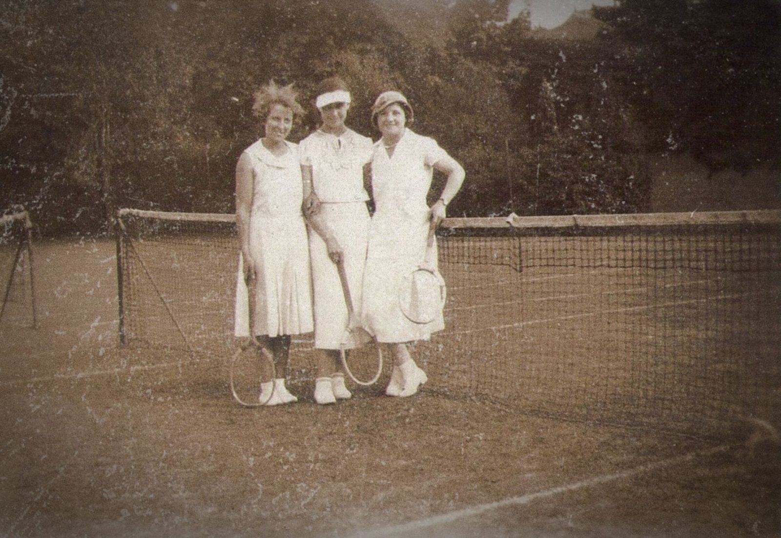 A vintage photograph of three women on a tennis court holding racquets