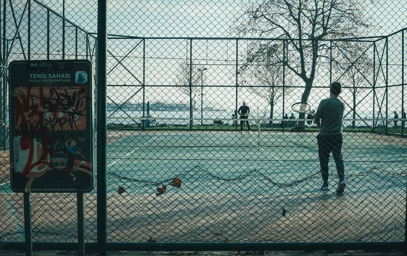 Two players in a match on an outdoor court with someone waiting at the side