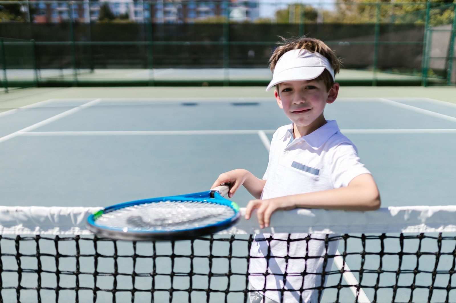 A smiling young boy in sportswear holding a tennis racquet on a sunny court